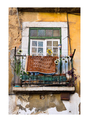 A carpet rug drying on a dilapidated balcony with sunflowers growing in a planter box. Lisbon, Lisboa, Portugal