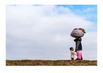 A mother carrying laundry on her head whilst leading her toddler past a brick foundry. Antananarivo, Madagascar.
