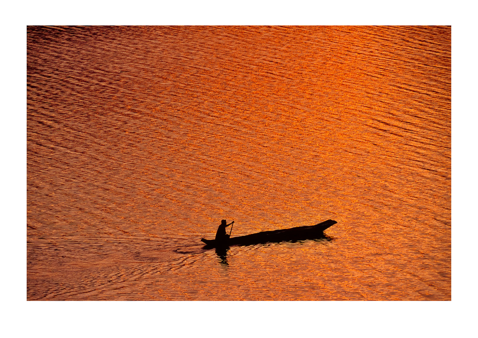 A fisherman in a dugout canoe on a golden lake surface at dawn. Lake Mutanda, Kisoro District, South Western Uganda.